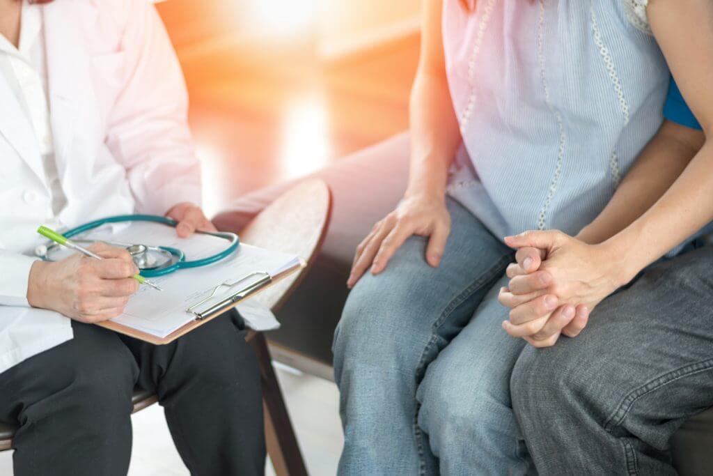 Person with a clipboard sitting next to two people holding hands